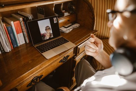 Consulta por vídeo em andamento na tela de um notebook, sobre escrivaninha de madeira em luz natural