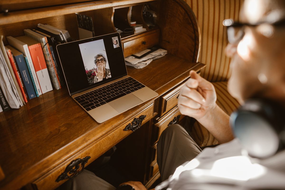 Consulta por vídeo em andamento na tela de um notebook, sobre escrivaninha de madeira em luz natural